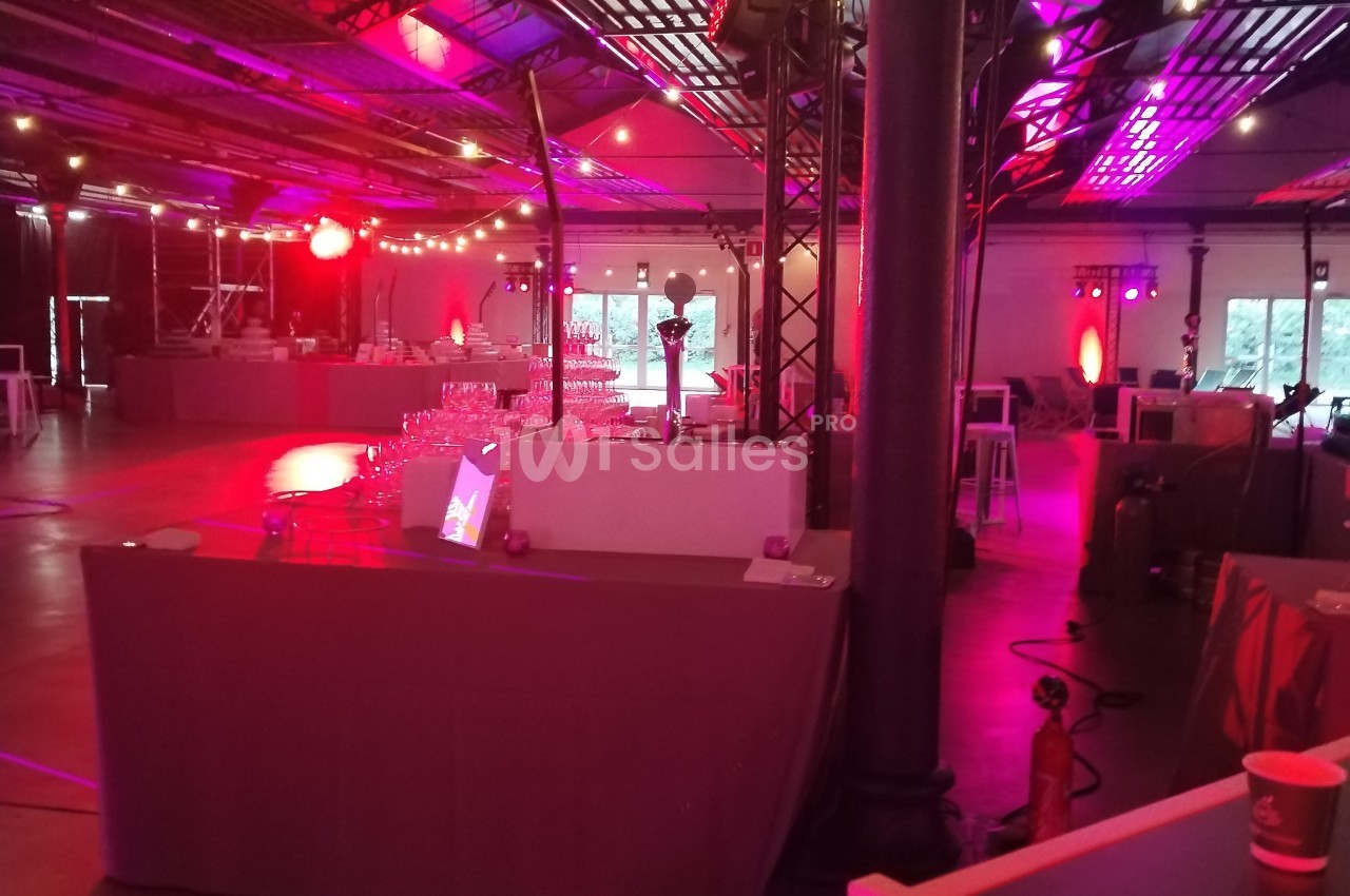 Salle de réception décorée avec des lumières colorées, des tables dressées et un éclairage tamisé.