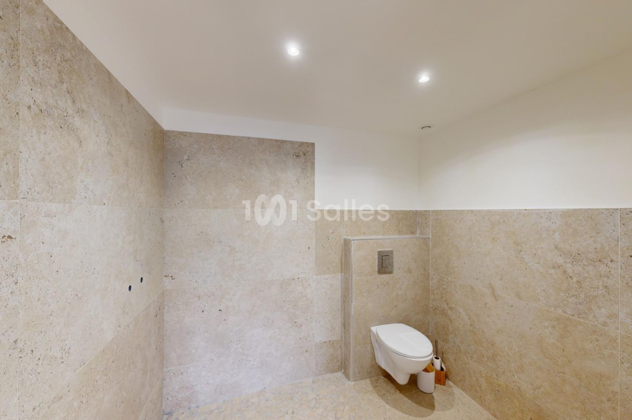 Toilettes modernes avec murs et sol en pierre beige, éclairage encastré et accessoires minimalistes.