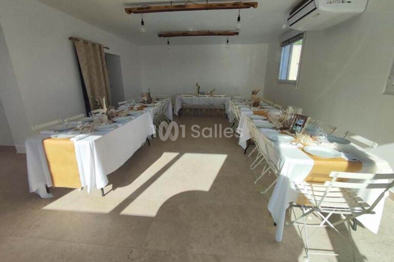 Salle lumineuse aménagée avec des tables dressées pour un repas, disposées en U, dans un décor sobre et moderne.