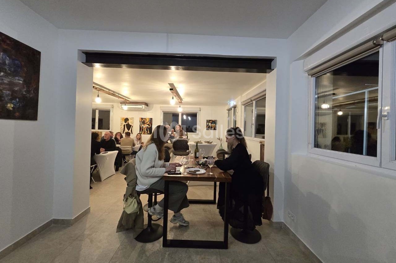 Deux personnes dînent à une table dans une salle lumineuse où d'autres convives sont rassemblés au fond.