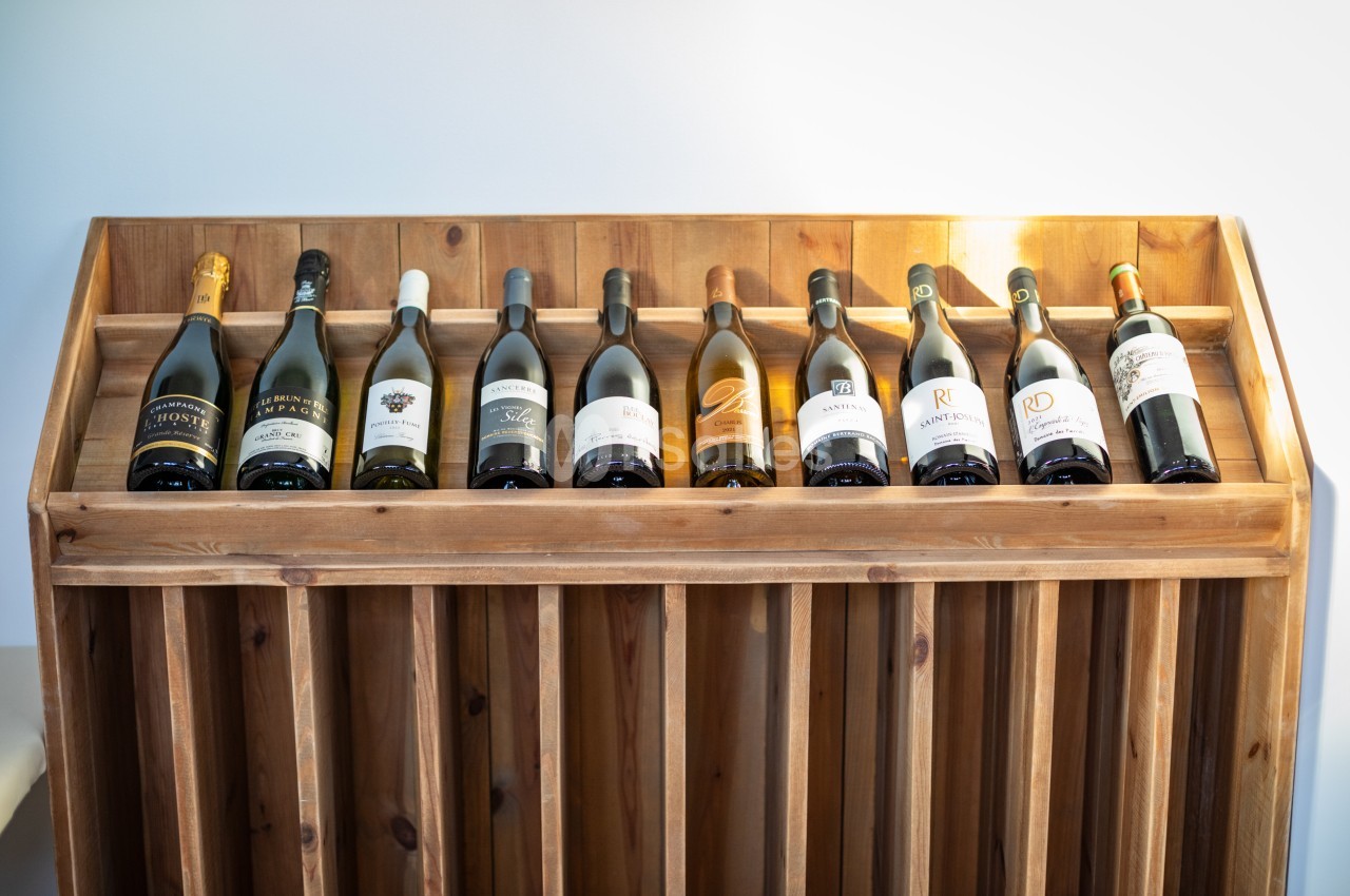 Bouteilles de vin alignées sur un présentoir en bois, éclairées par une lumière naturelle.