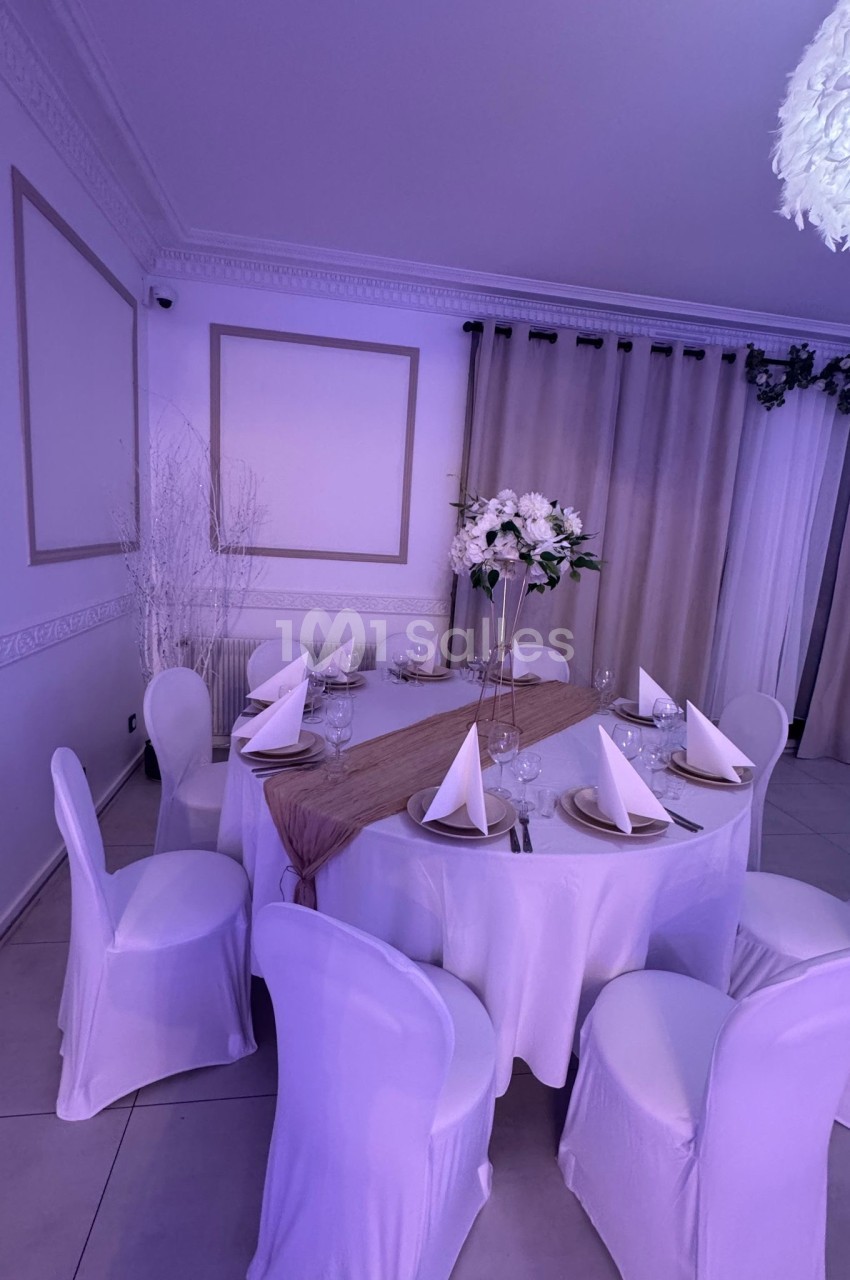 Table ronde élégamment dressée avec nappes blanches, serviettes pliées, vaisselle et centre de table floral dans une salle…