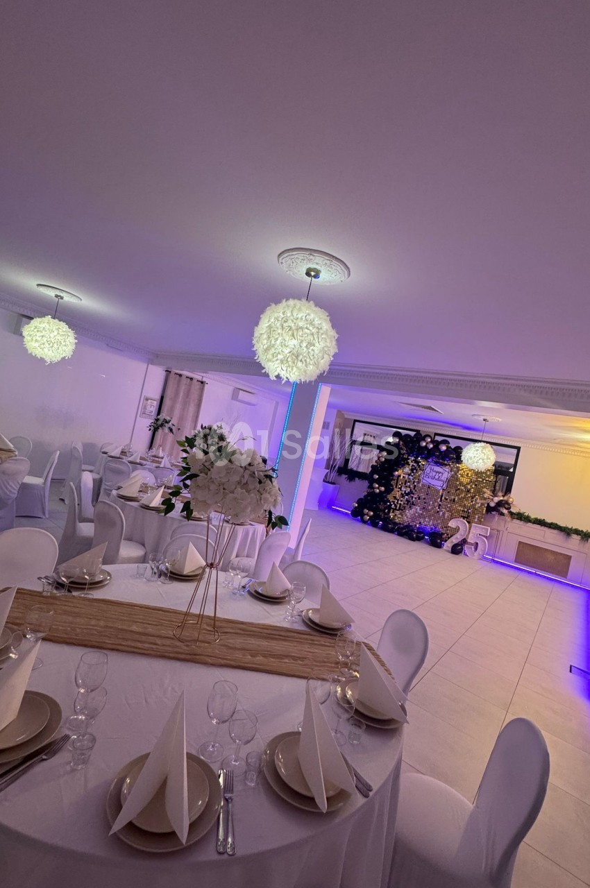 Salle de réception décorée avec des tables dressées, des chaises blanches et un espace lumineux avec éclairage violet.