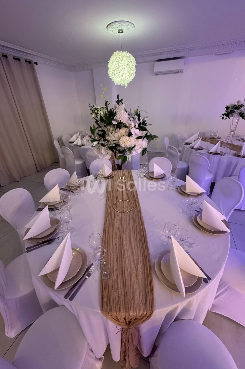Table ronde décorée pour un événement, avec nappes blanches, serviettes pliées, vaisselle élégante et centre floral.