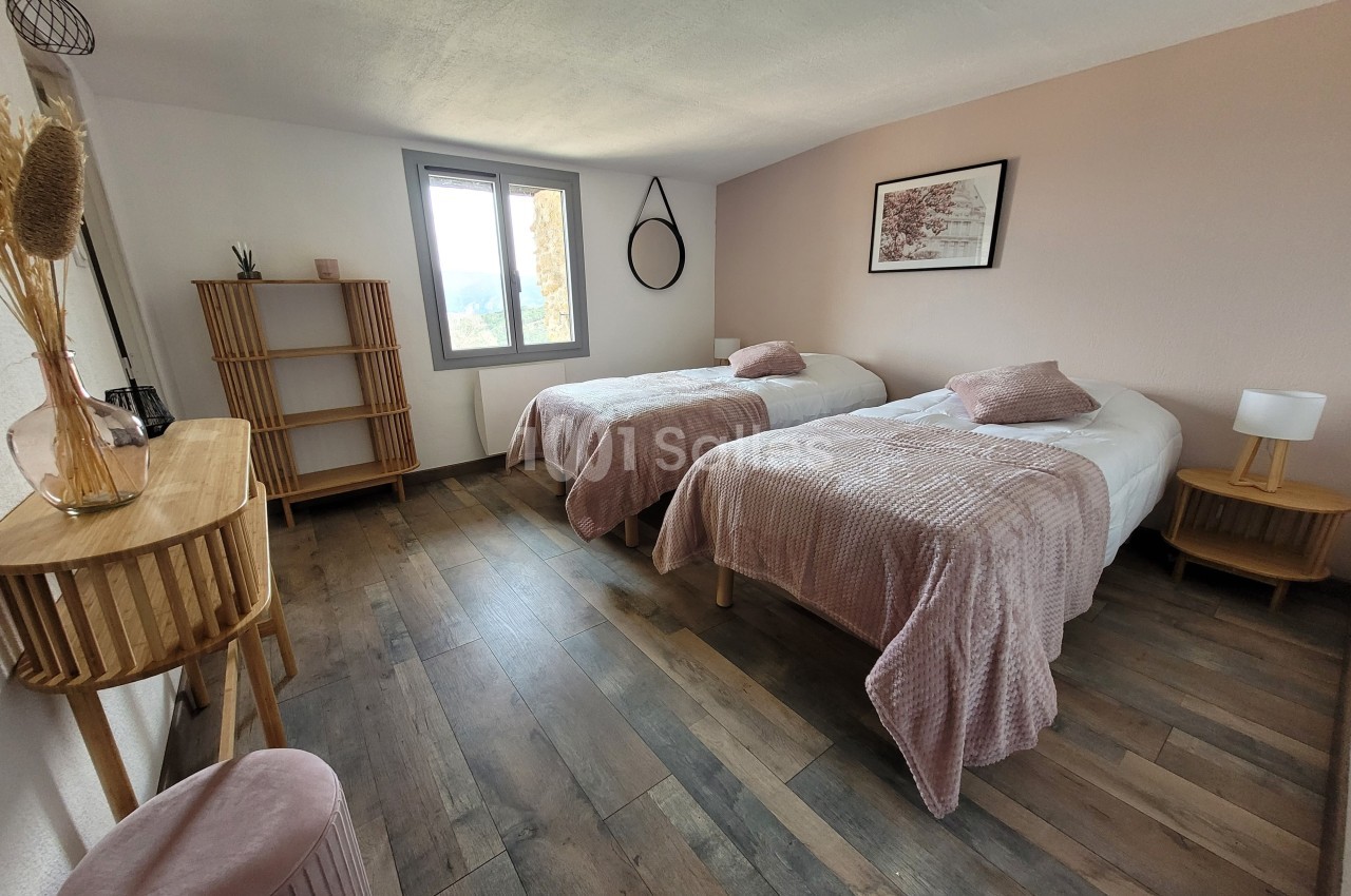 Chambre lumineuse avec deux lits simples, décoration sobre, murs clairs et mobilier en bois.