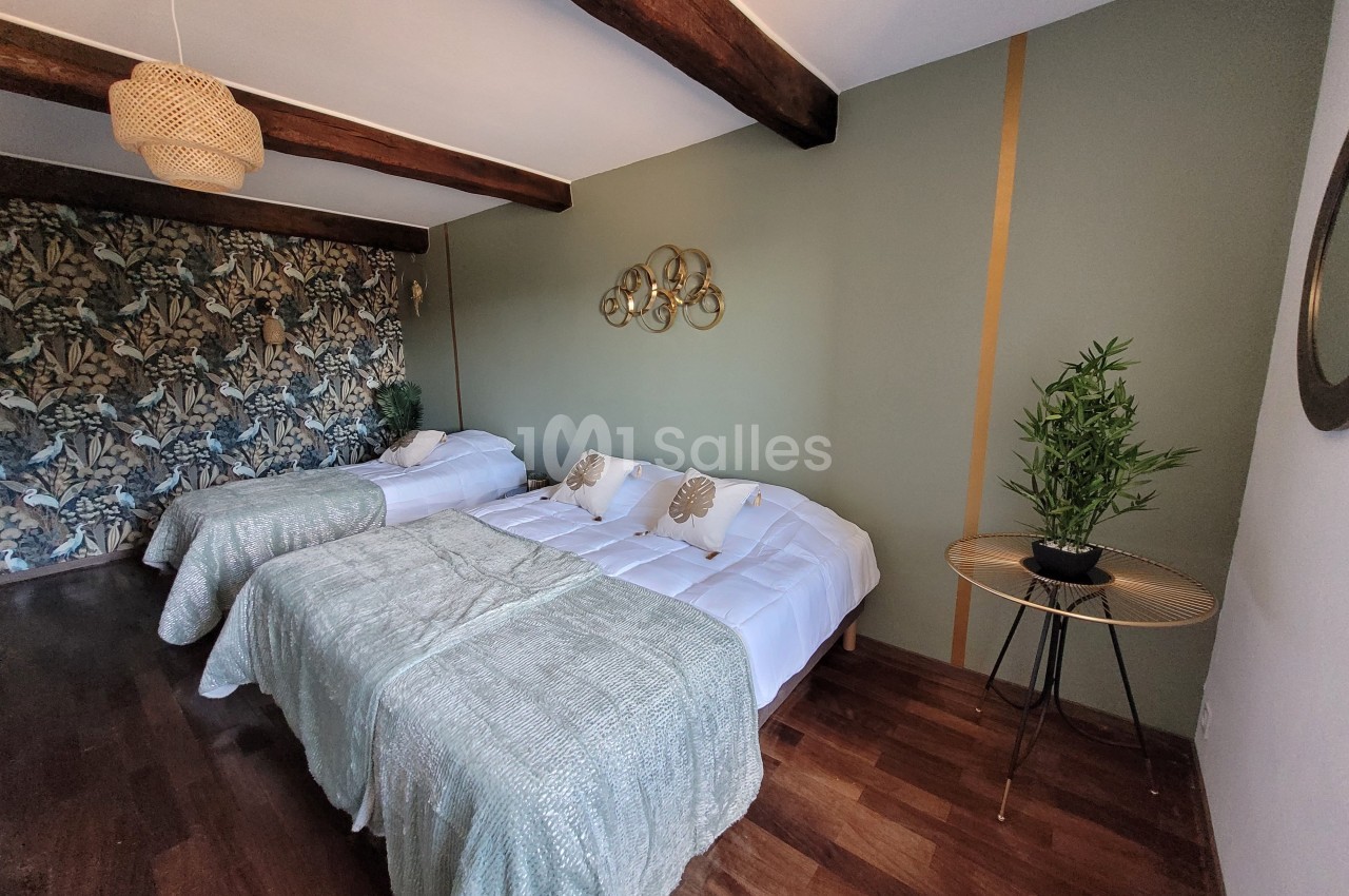 Chambre avec deux lits doubles, parquet, mur vert orné, papier peint floral et décoration végétale.
