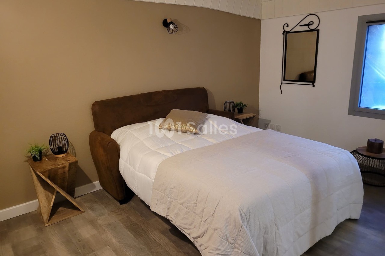 Lit double avec couverture blanche dans une chambre au mur beige, décorée de tables de chevet et d'un miroir mural.