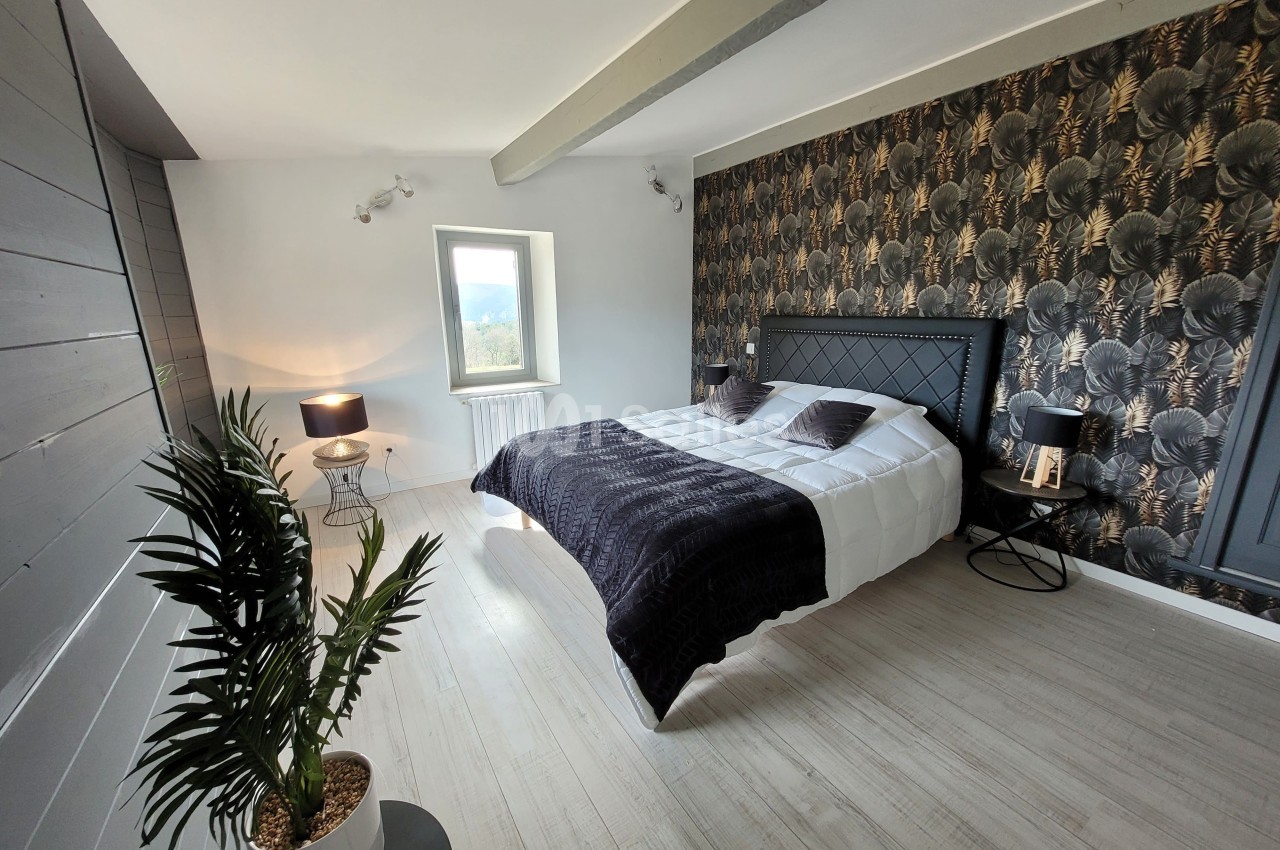 Chambre lumineuse avec lit double, mur décoré de papier peint floral sombre, lampe et plante en pot.
