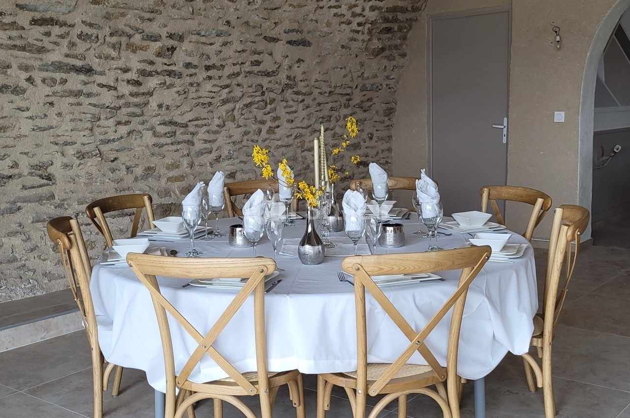 Table ronde dressée avec une nappe blanche, vaisselle élégante, serviettes pliées et décoration florale jaune.