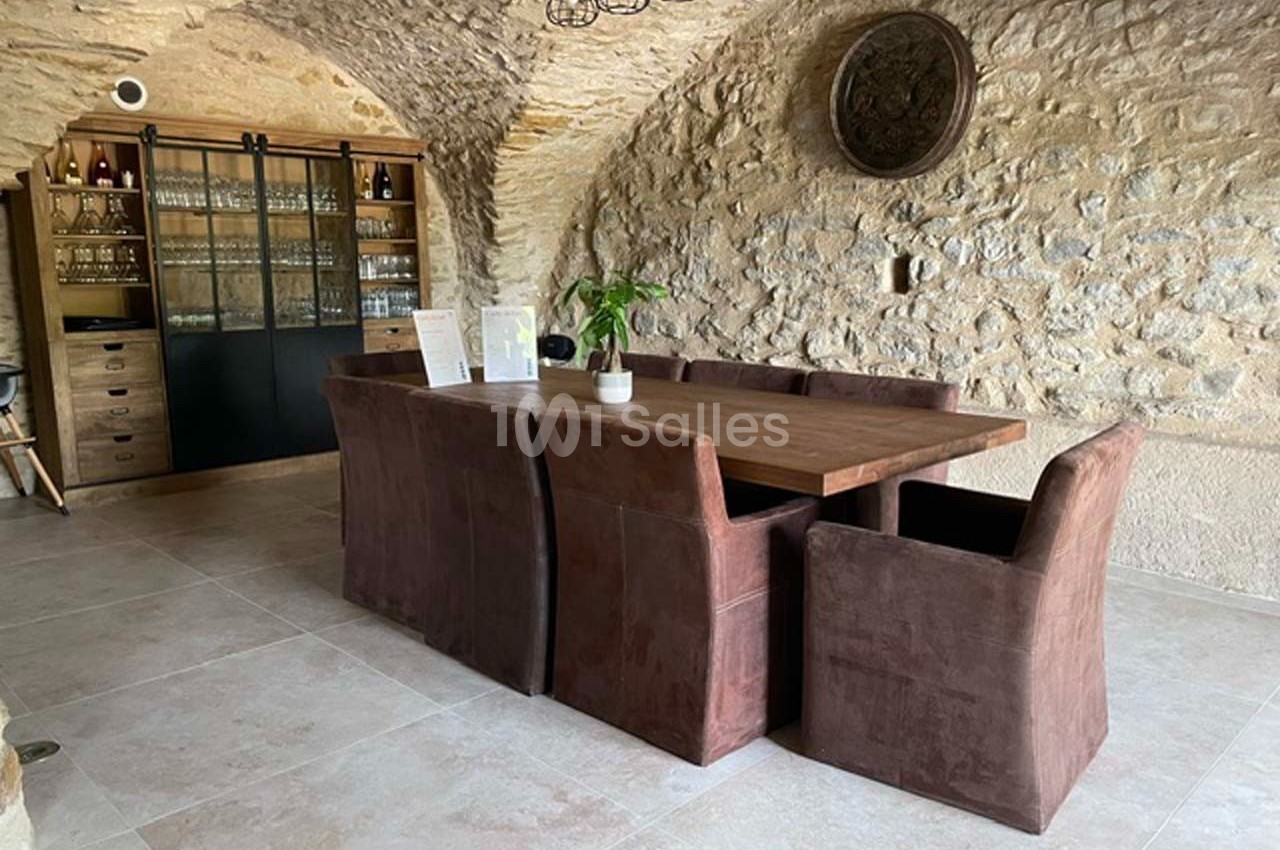 Salle à manger avec table en bois, chaises marron, murs en pierre apparente et meuble vitré en arrière-plan.