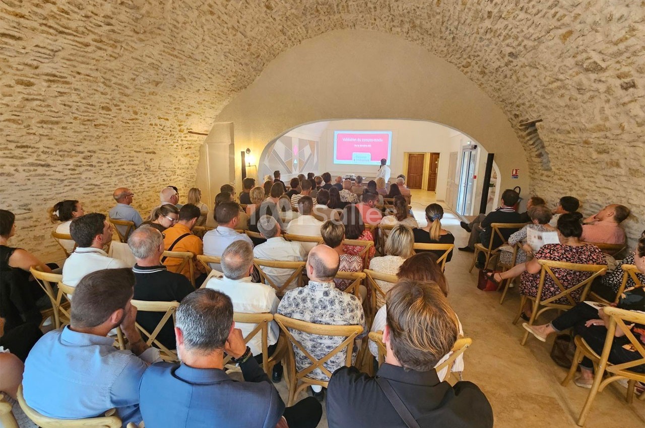 Salle voûtée en pierre avec des personnes assises assistantes à une présentation projetée sur un écran.