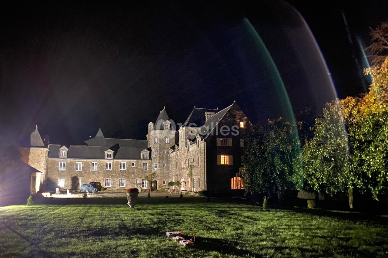 Façade éclairée d'un grand bâtiment en pierre de style ancien, entouré d'une pelouse, de nuit.