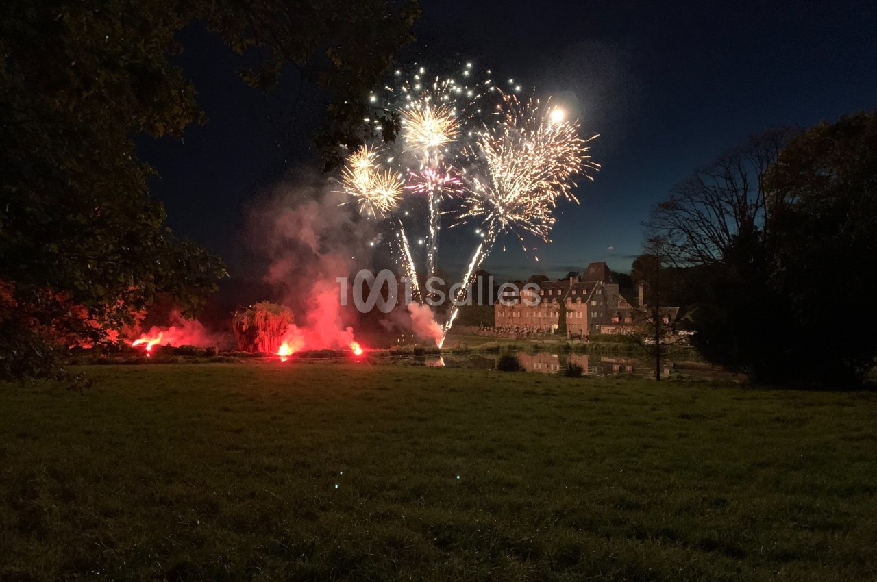 Feu d'artifice illuminant le ciel nocturne au-dessus d'un bâtiment en briques, entouré d'arbres et d'une pelouse.