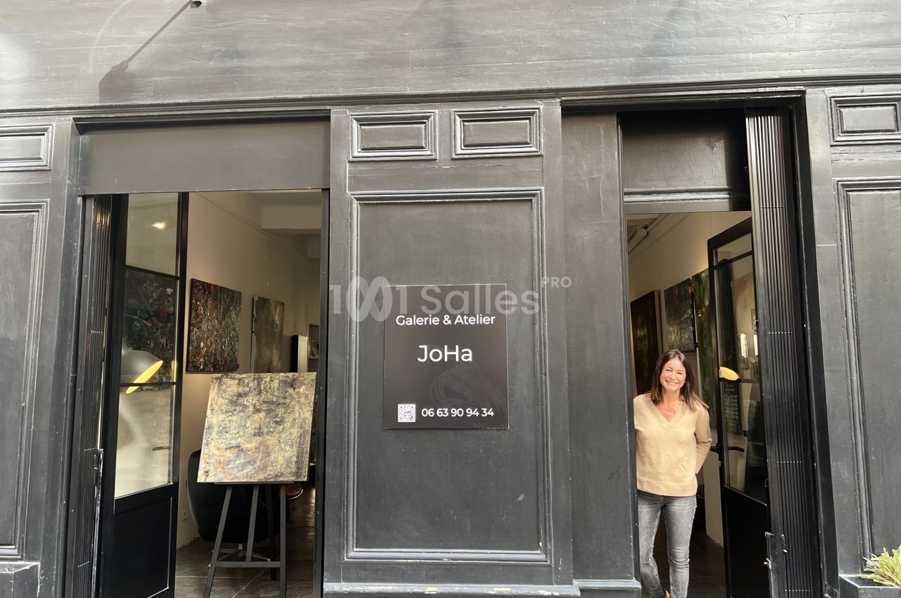Façade d'une galerie d'art avec une femme souriante debout dans l'encadrement de la porte.