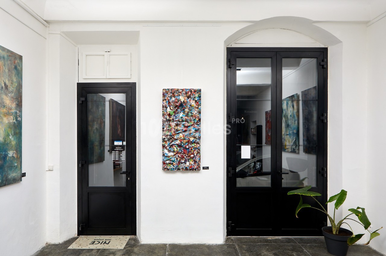 Vue intérieure d'une galerie avec un tableau abstrait coloré accroché sur un mur blanc entre deux portes vitrées.