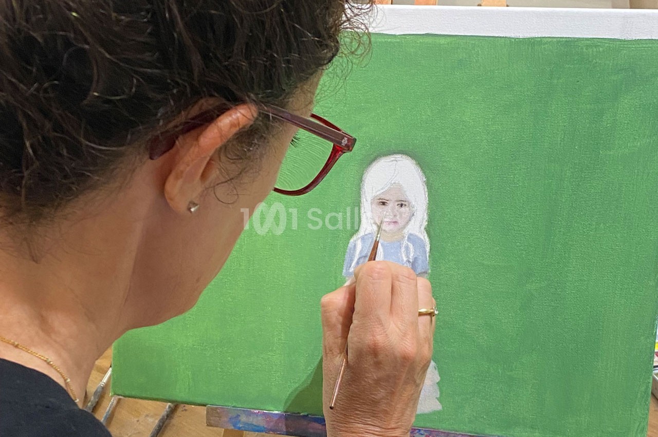 Une femme peint une petite fille en robe bleue sur une toile avec un fond vert.