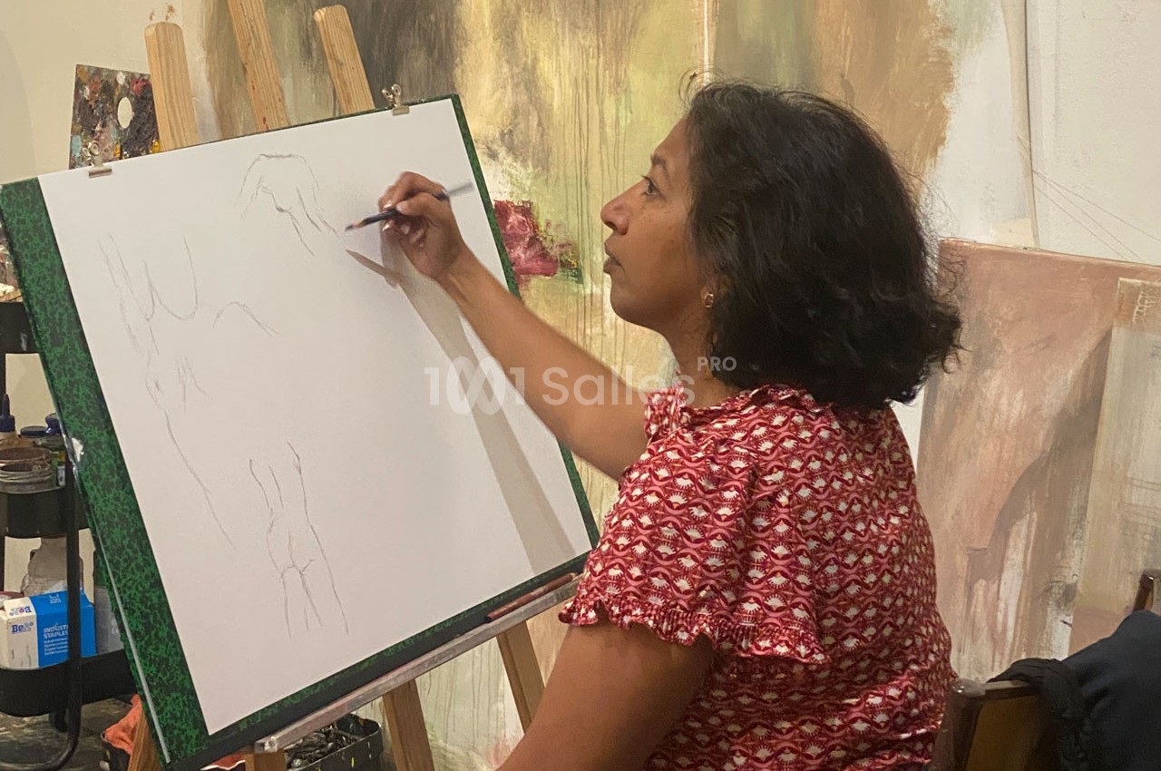 Une femme dessine sur une toile blanche posée sur un chevalet dans un atelier d'art.