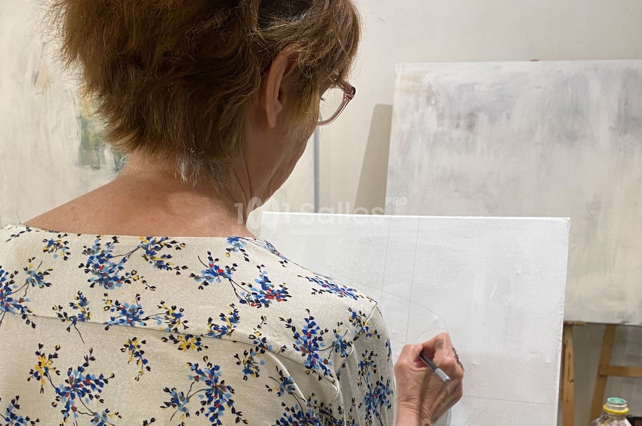 Femme de dos, dessinant sur une toile blanche dans un atelier lumineux.