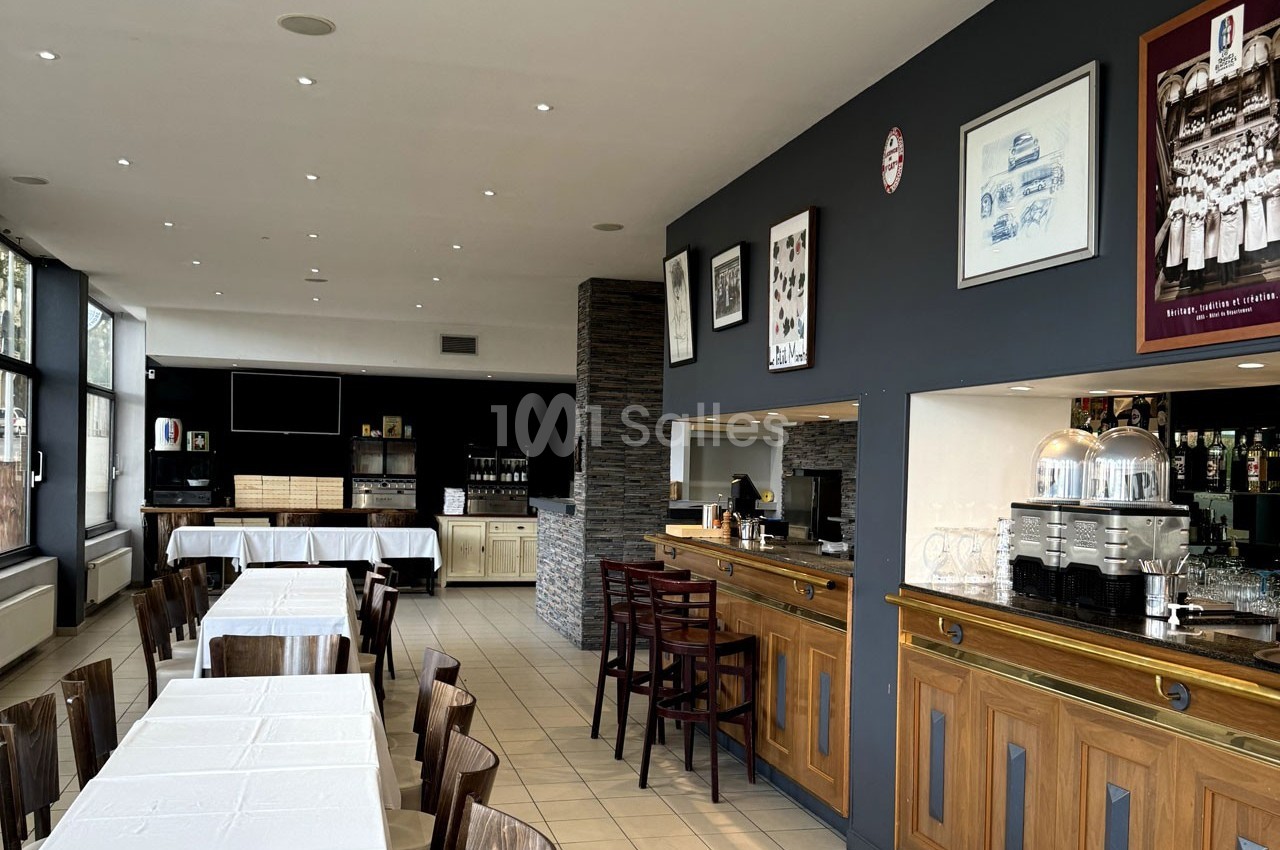 Salle de restaurant lumineuse avec tables dressées, bar en bois, machine à café et décorations murales.