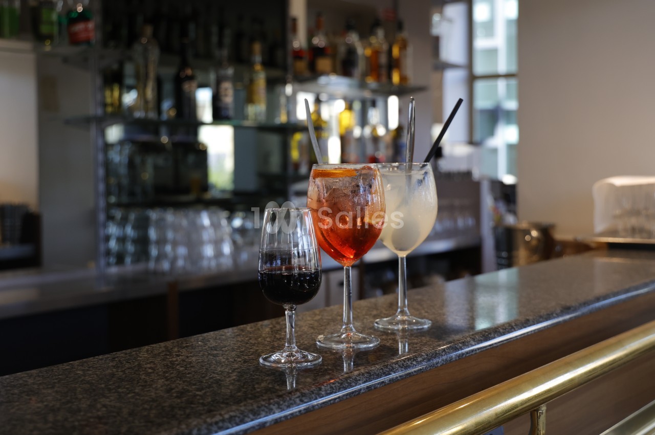 Trois verres de boissons variées posés sur un comptoir de bar, avec des bouteilles en arrière-plan.