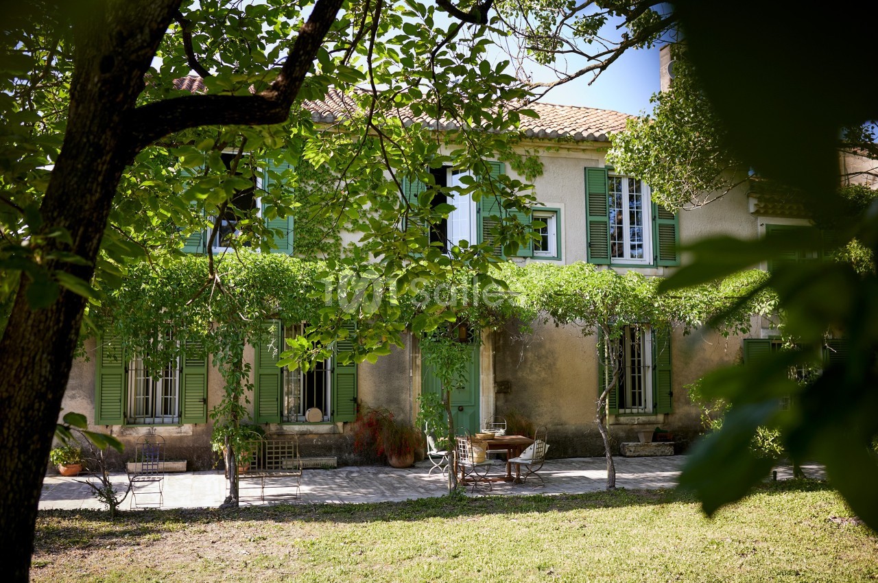 Façade d'une maison provençale avec volets verts, terrasse ombragée et végétation environnante.