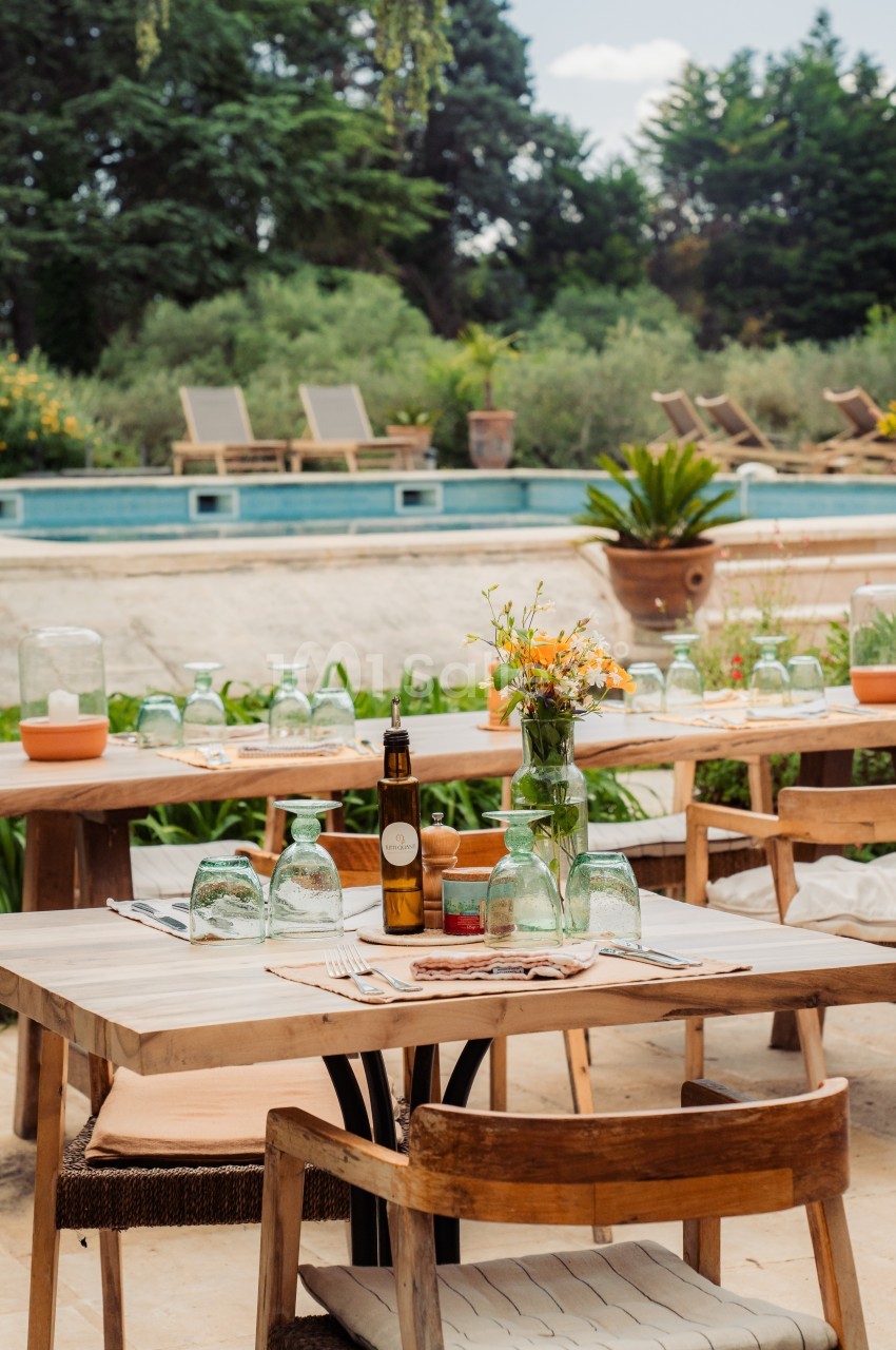 Tables en bois dressées en extérieur près d'une piscine, entourées de verdure et de chaises longues.
