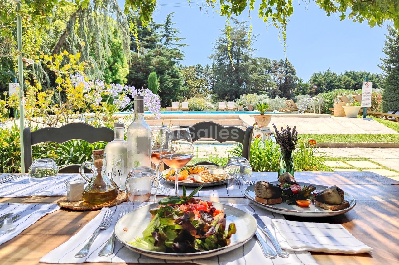 Table dressée en extérieur avec des assiettes de plats variés, vue sur un jardin verdoyant et une piscine en arrière-plan.