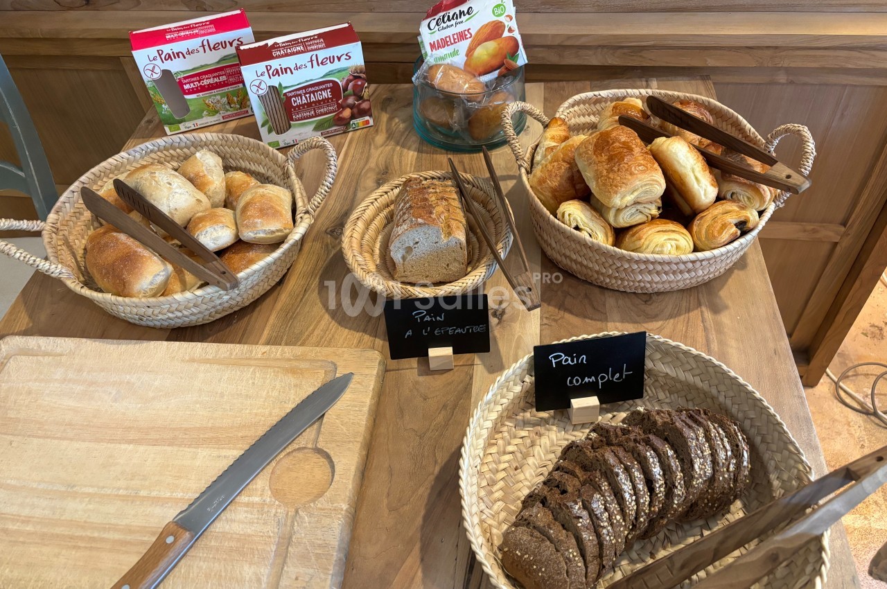 Buffet de petits-déjeuners avec paniers de viennoiseries, pains variés, couteaux et planche en bois.