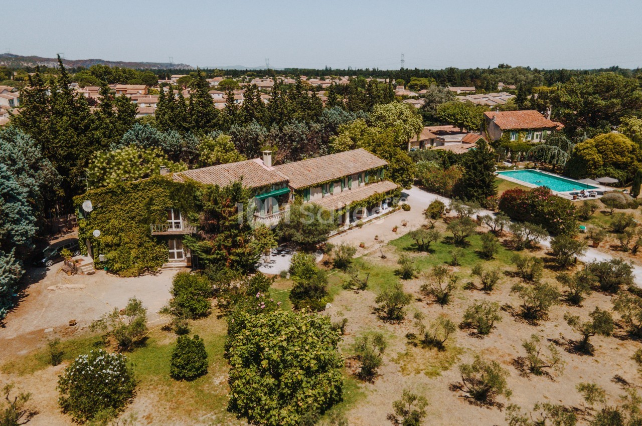 Vue aérienne d'une maison entourée d'arbres, avec une piscine et un jardin dans un environnement rural.