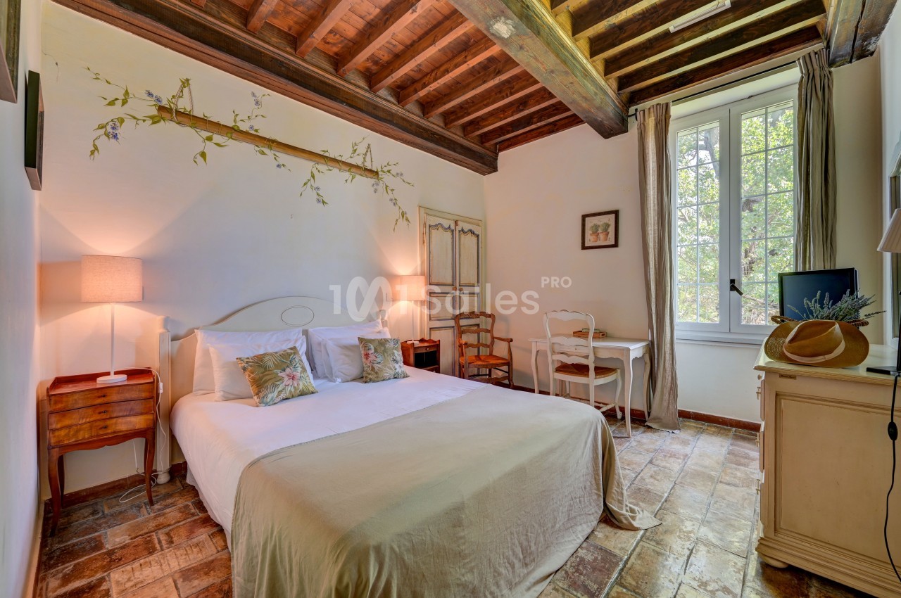 Chambre lumineuse avec lit double, poutres apparentes, bureau près d'une fenêtre et décoration naturelle.