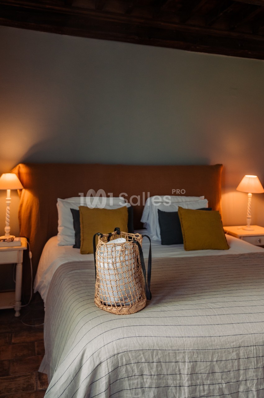 Lit double avec tête de lit orange, tables de chevet, lampes allumées et un sac en osier posé sur le couvre-lit.