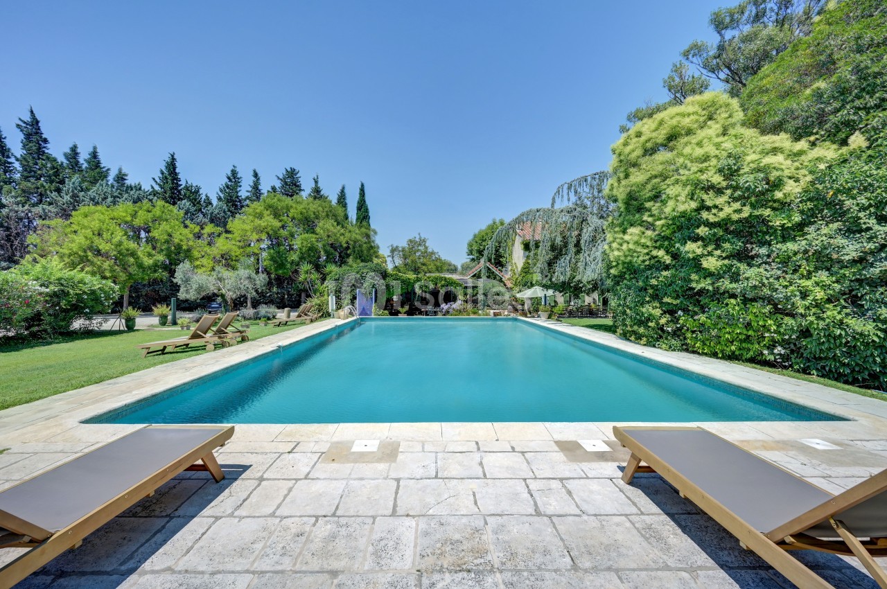 Piscine extérieure entourée de végétation luxuriante, avec transats en bois sur une terrasse en pierre.