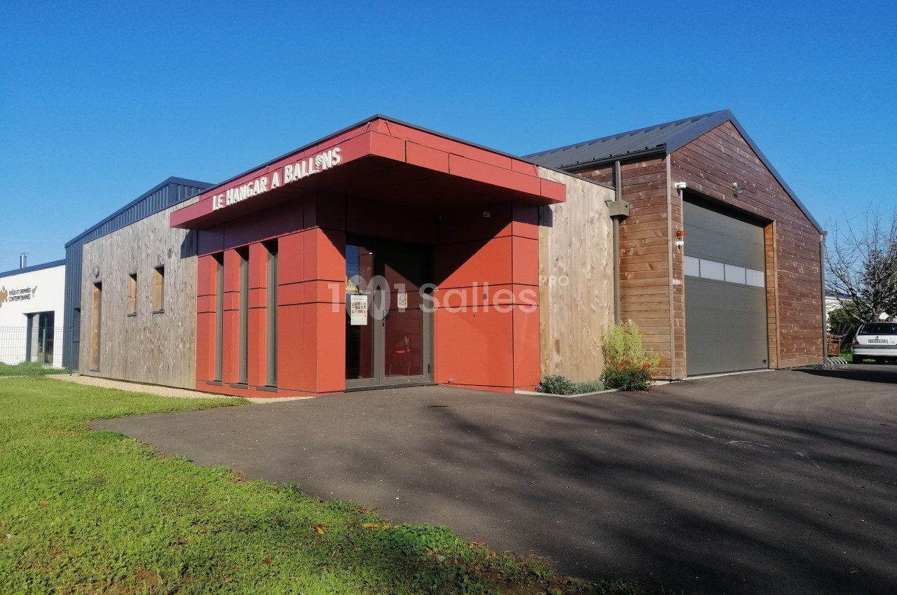 Bâtiment moderne avec façade en bois et rouge, entrée vitrée et grande porte de garage sur la droite.