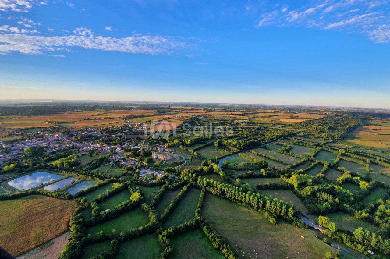 Vue aérienne d'une campagne verdoyante avec champs, haies, étangs et un village sous un ciel bleu dégagé.