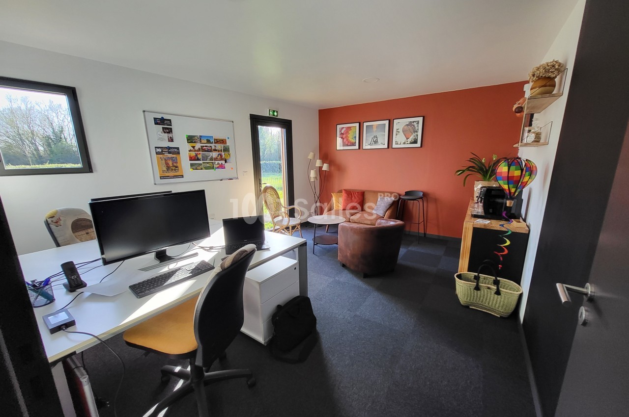 Bureau lumineux avec poste de travail, fauteuils, mur orange décoré et étagères, vue sur l'extérieur.