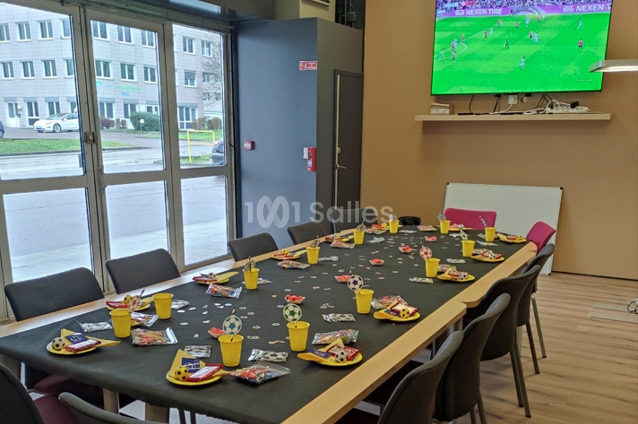 Table décorée sur le thème du football avec assiettes et gobelets, écran diffusant un match en arrière-plan.