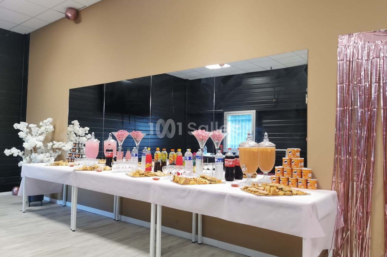 Table garnie de boissons, pâtisseries et friandises dans une salle décorée avec des tons roses et beige.