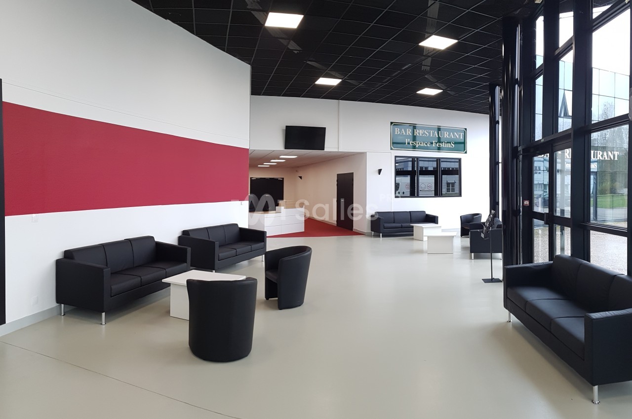 Espace d'accueil moderne avec canapés noirs, tables basses blanches et grande baie vitrée laissant entrer la lumière.