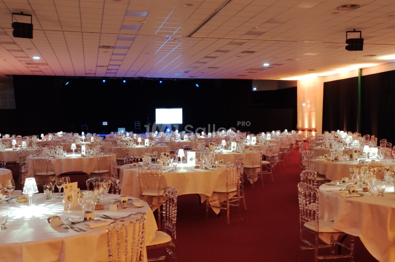 Salle de réception avec tables rondes dressées, chaises transparentes et éclairage tamisé.