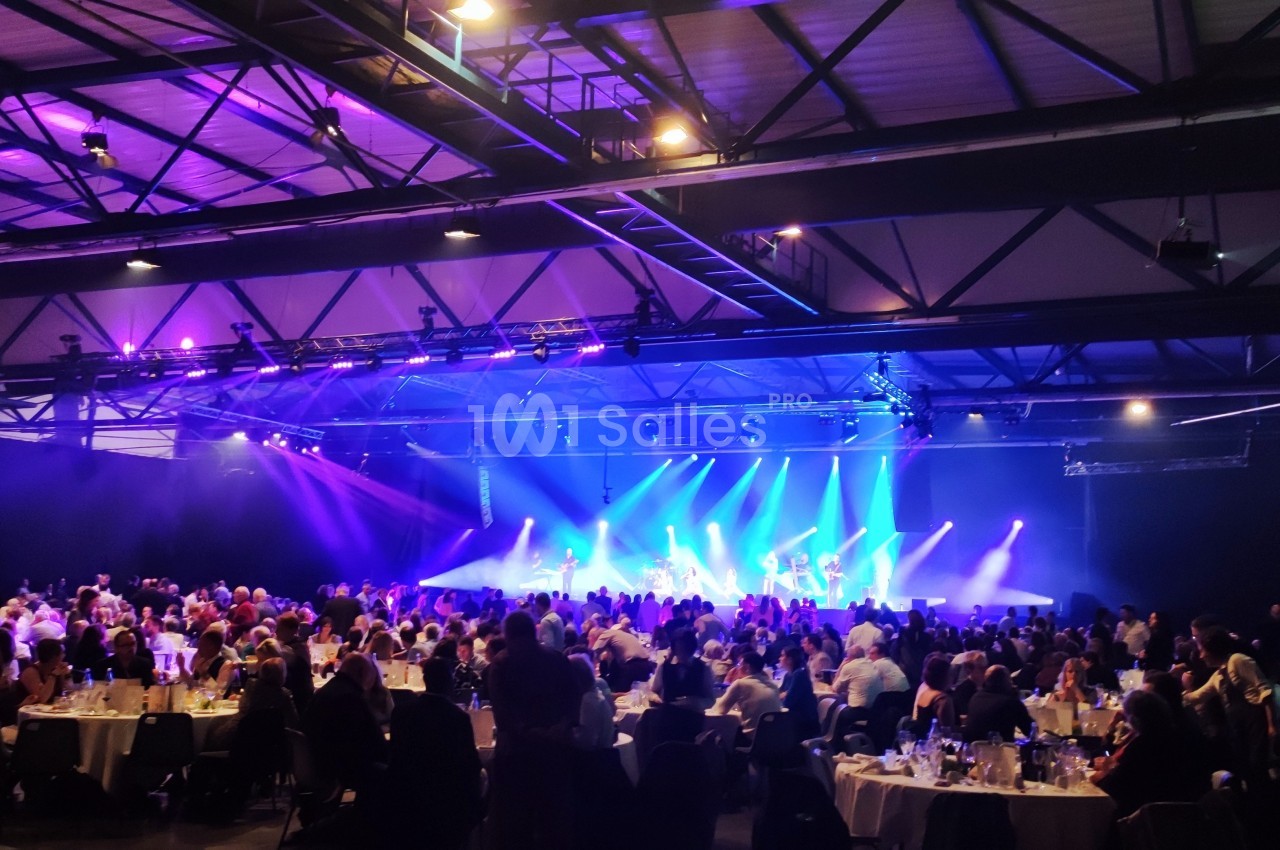 Salle de spectacle avec des tables occupées par des spectateurs et une scène illuminée par des projecteurs colorés.