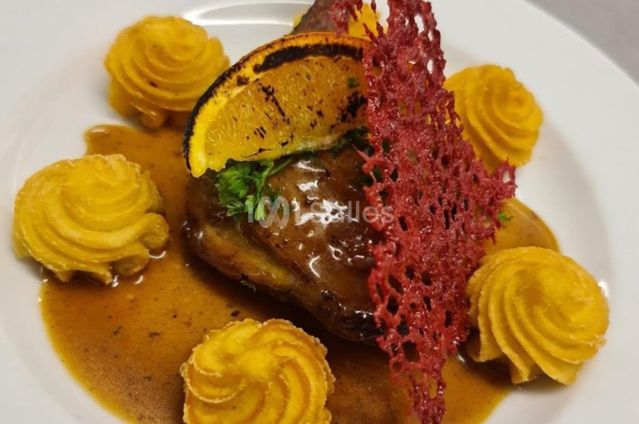 Assiette gastronomique avec viande en sauce, purée en rosaces, tranche d'orange grillée et tuile rouge décorative.