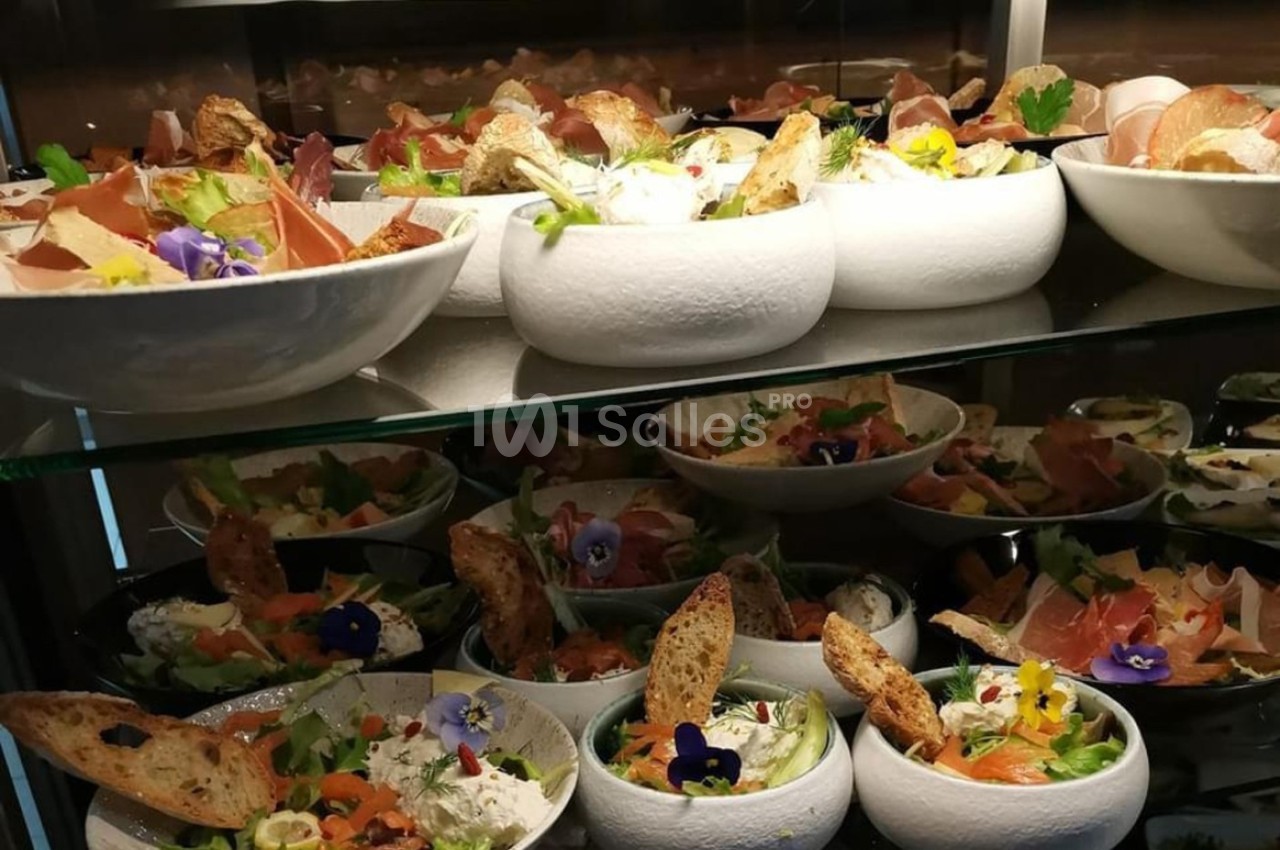 Assortiment de salades garnies de légumes, fleurs comestibles, pain grillé et charcuterie, disposées sur des étagères.