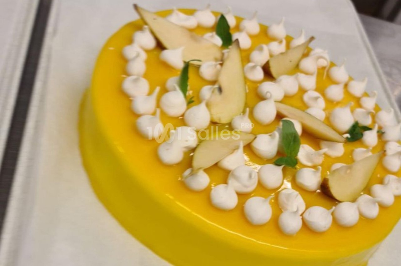 Gâteau rond avec glaçage jaune, décoré de meringues blanches, tranches de poire et feuilles vertes.