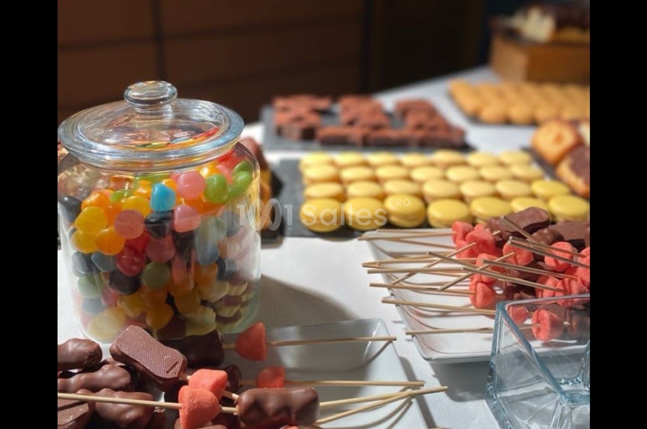 Bocal de bonbons colorés, macarons jaunes et brochettes de friandises disposés sur une table de buffet.