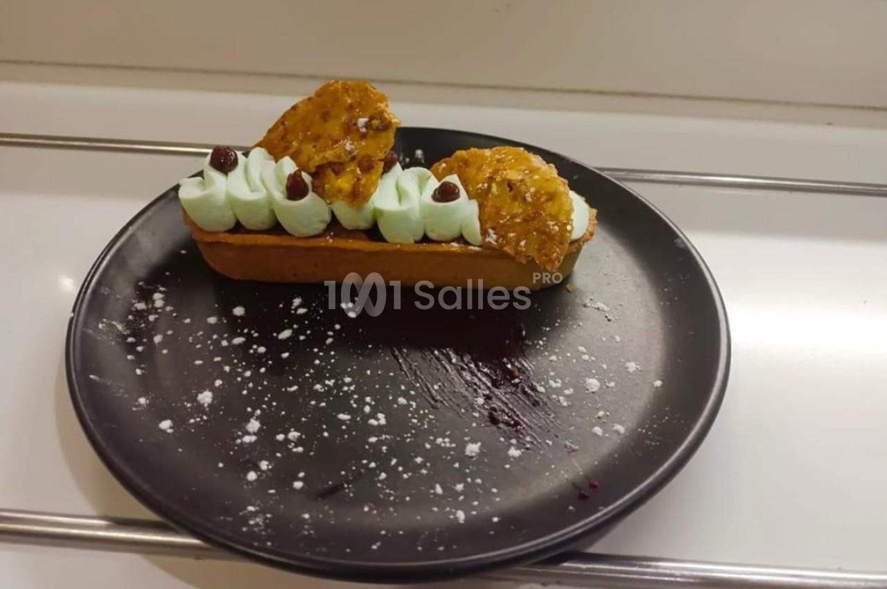 Tartelette garnie de crème verte, décorée de biscuits croquants et de petites baies, présentée sur une assiette noire.