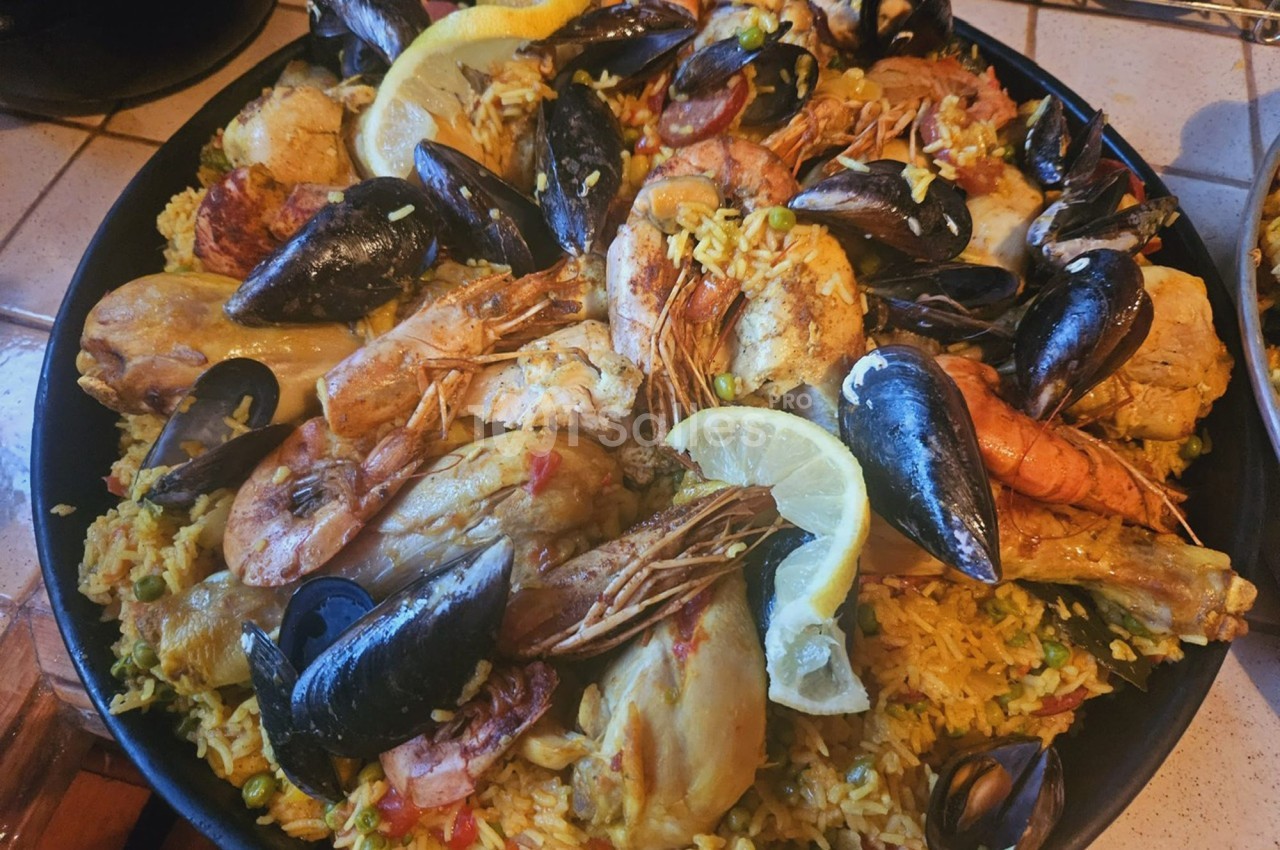 Plat de paella garni de fruits de mer, poulet, légumes et tranches de citron, présenté dans une grande poêle.