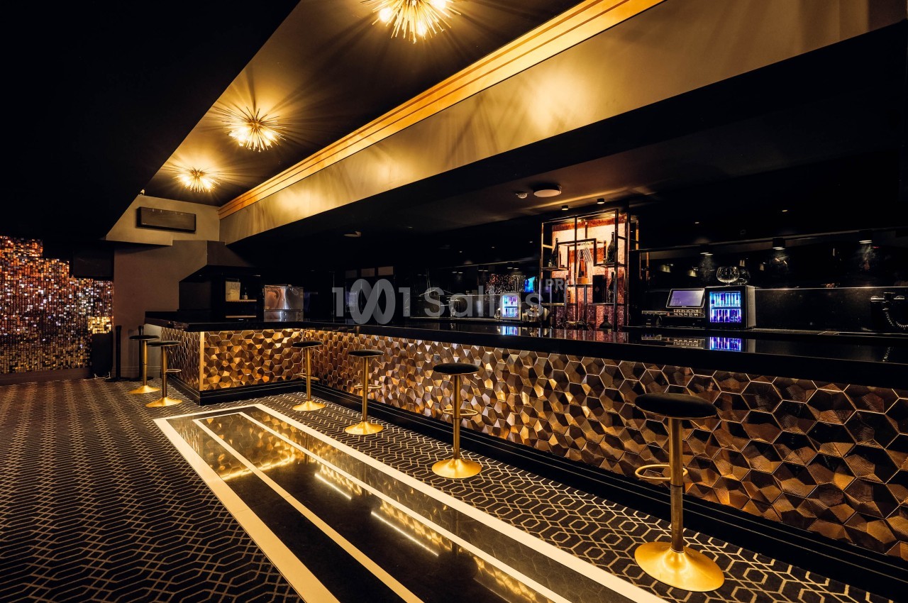 Intérieur d'un bar élégant avec comptoir doré, tabourets hauts et éclairage tamisé.
