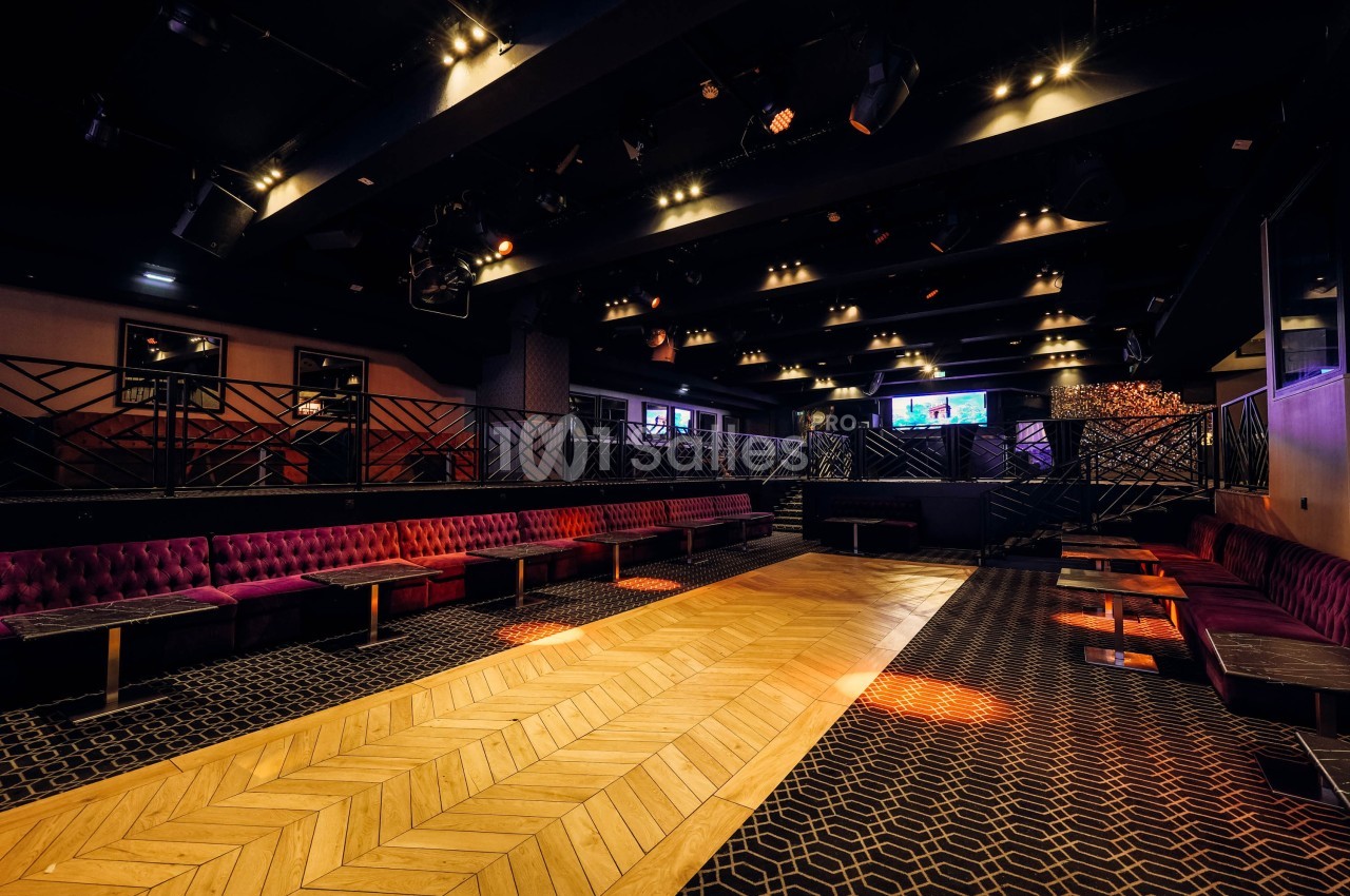 Salle vide avec parquet central, banquettes rouges sur les côtés et éclairage tamisé dans une ambiance de club.