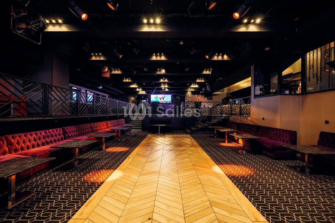 Salle de réception moderne avec banquettes rouges, tables en marbre et parquet clair, éclairée par des spots.