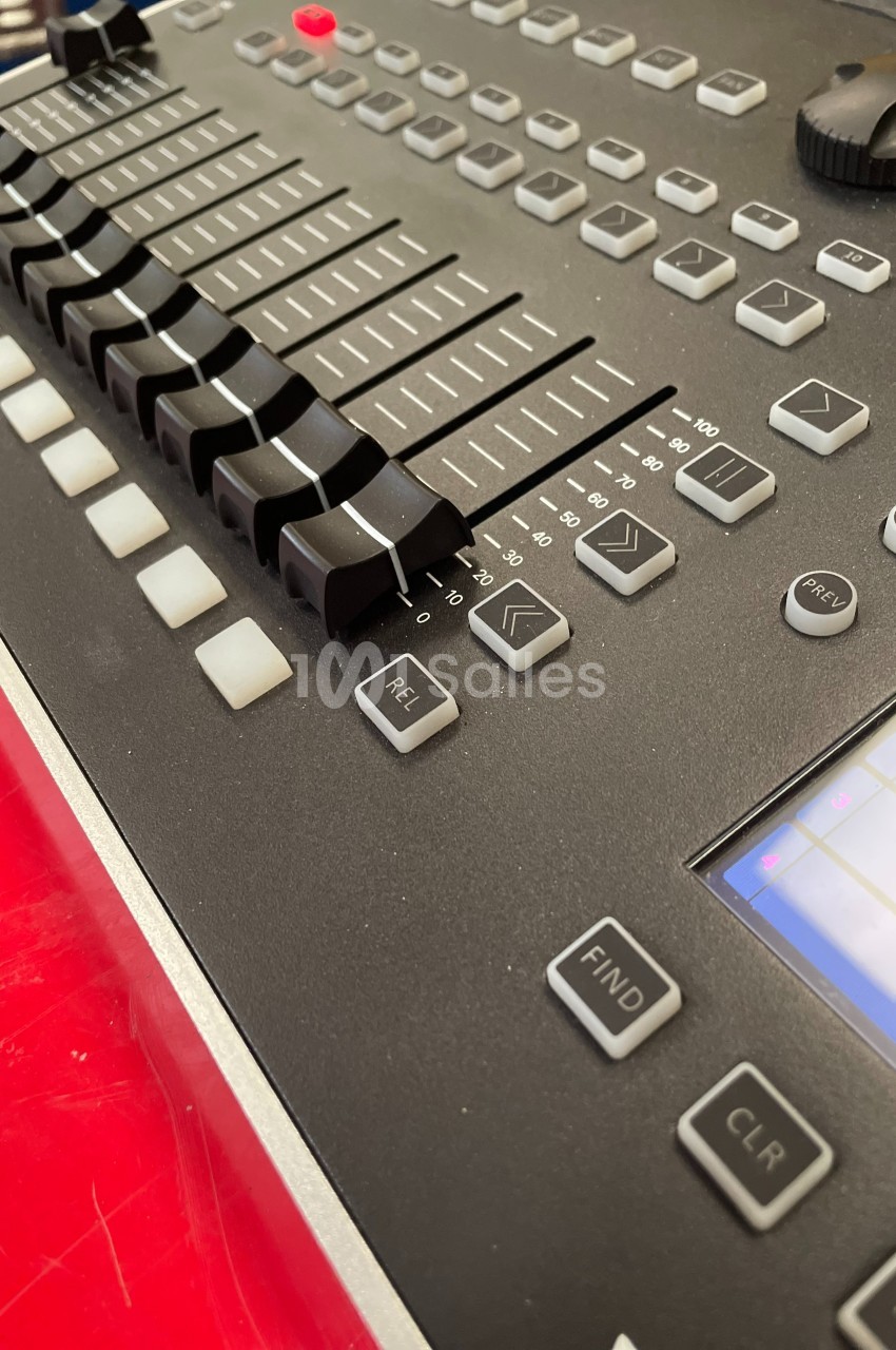 Table de mixage audio avec curseurs, boutons et écran tactile, posée sur une surface rouge.